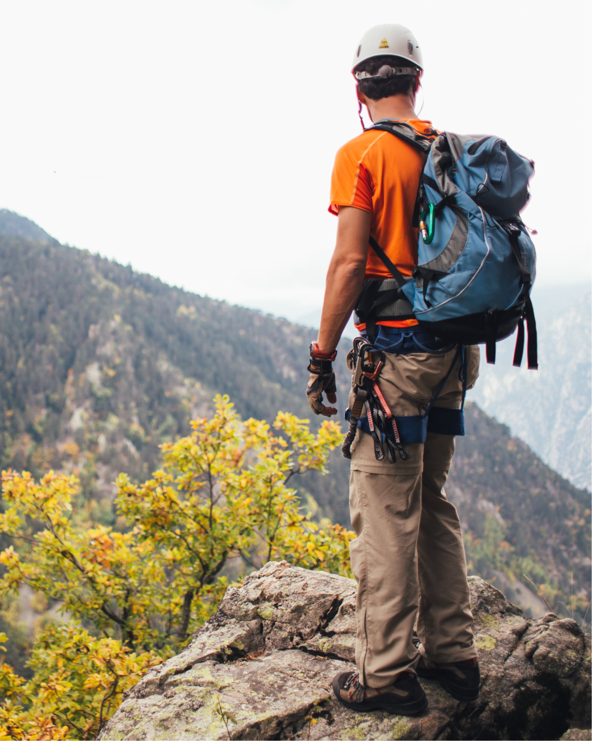 Hiker with a backpack standing on a rocky outcrop overlooking a mountainous landscape.